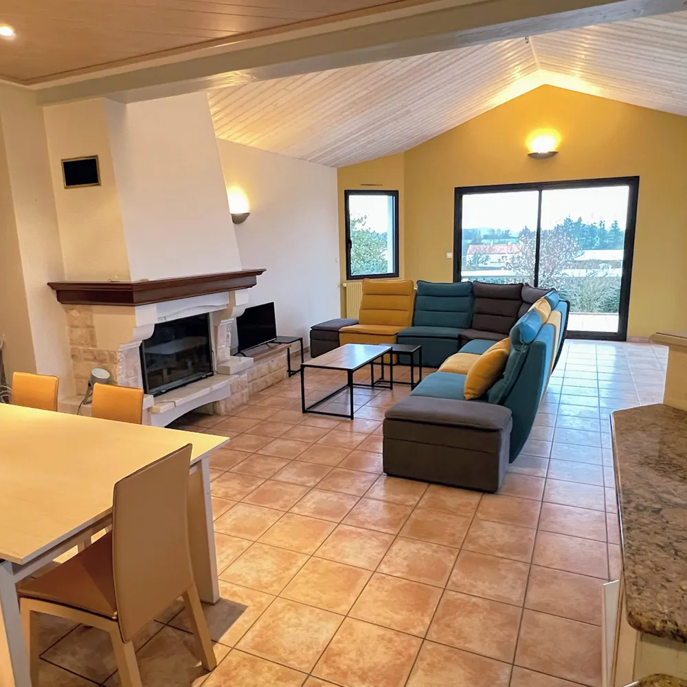 Grand séjour lumineux avec cheminée, canapé d'angle et baies vitrées au Gîte du Coteau